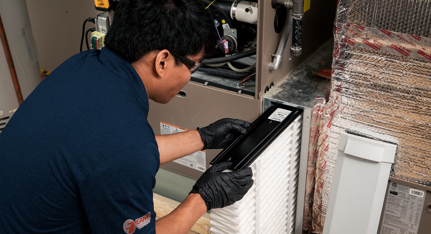 A professional Eanes HVAC technician replacing a clean pleated air filter in an indoor air handler unit during a routine AC maintenance tune-up.