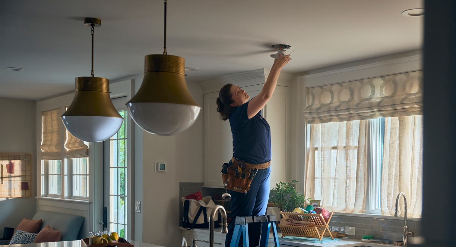 A professional Eanes electrician standing on a ladder to install modern recessed ceiling lights during a residential electrical installation service.
